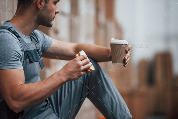 Storage worker sits and have a break. Eats sandwitch and drinks coffee