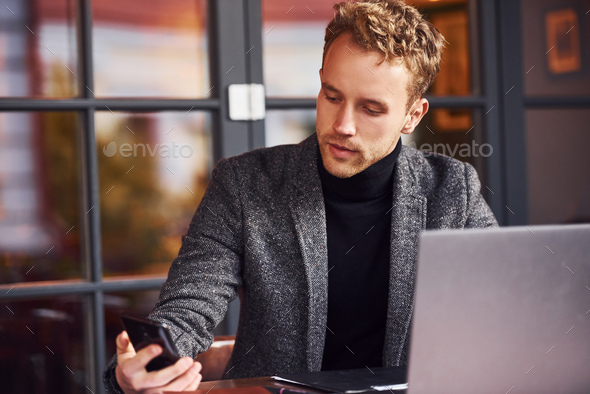 Elegant young guy in formal wear sits in cafe with his laptop