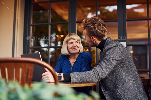 Young guy in formal clothes have a business talk with old woman in cafe