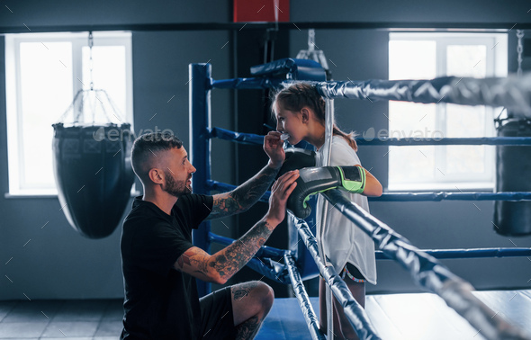 Conception of assistance. Young tattooed boxing coach teaches cute little girl in the gym
