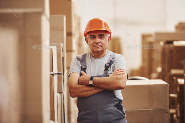 Portrait of senior storage worker in warehouse in uniform and hard hat
