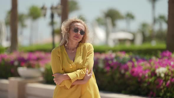 a Curlyhaired Blonde in Sunglasses and a Yellow Dress Poses Against the Background of a Blurred alt
