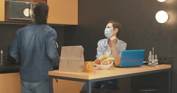 Interracial Couple in Covid-19 Face Masks Talking in Kitchen at Home. Confident Caucasian Woman and alt
