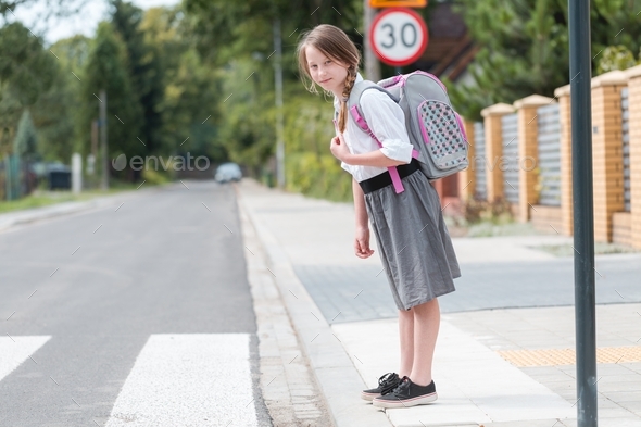 Adorable girl and is standing in front of a pedestrian crossing on a one-way street