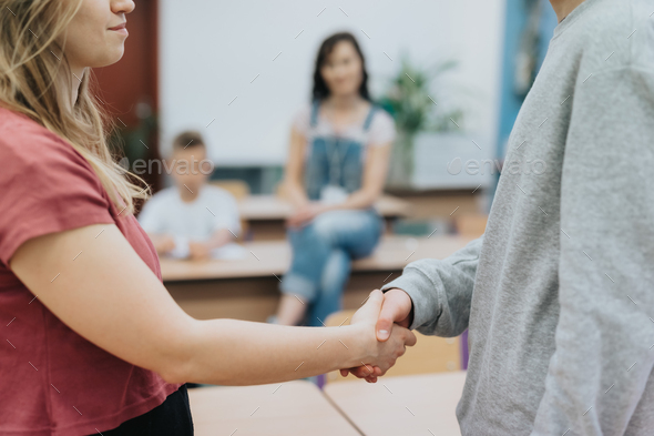 Two friends at odds shake hands during a workshop with a psychologist at school