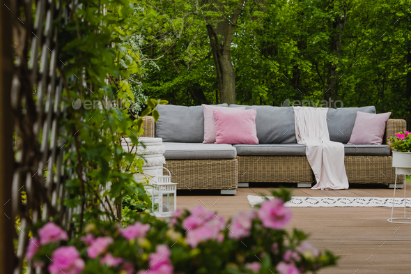 Pastel pink pillows on grey sofa in green garden with wooden terrace
