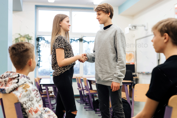 Two friends at odds shake hands during a workshop with a psychologist at school