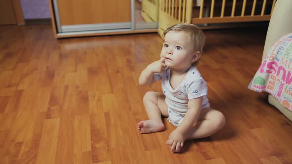 Baby boy sitting on the floor in the room. alt