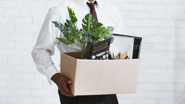 Losing job. Closeup view of African American guy with box of his stuff leaving office