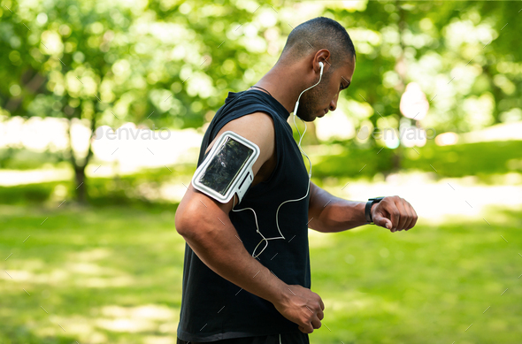 Side view of African American guy checking health data on smartwatch after jogging at park