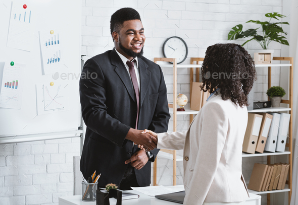 Joyful HR manager shaking hands with millennial applicant at job interview at company office