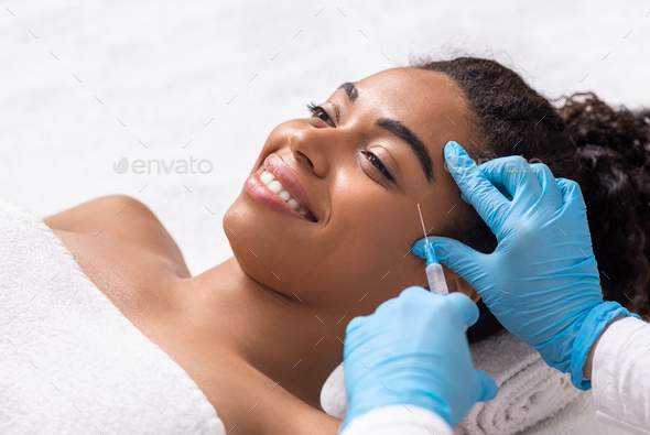 Smiling black woman having anti-aging injection for eye zone