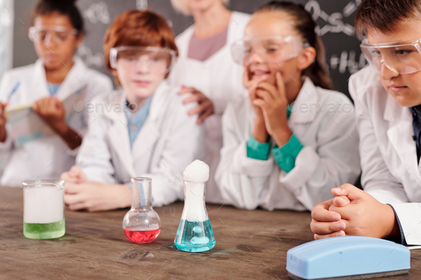 Three glass tubes with chemical compounds standing on teacher desk in lab