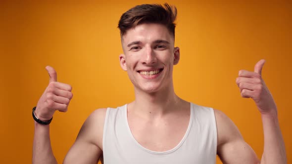 Surprised Young Man Showing Thumbs Up Against Yellow Background in Studio