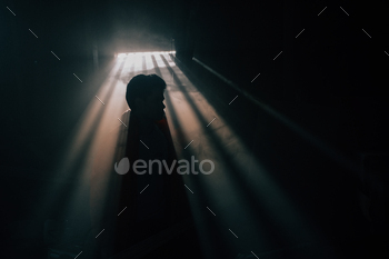 A man silhouetted against a window with sunshine pouring through in a dark room