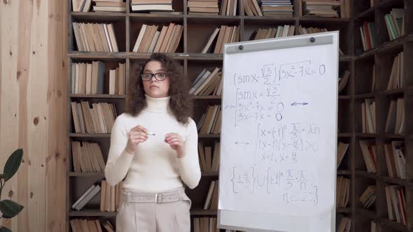 Confident Hispanic Young Woman Math Teacher Giving Class Pointing at Whiteboard alt