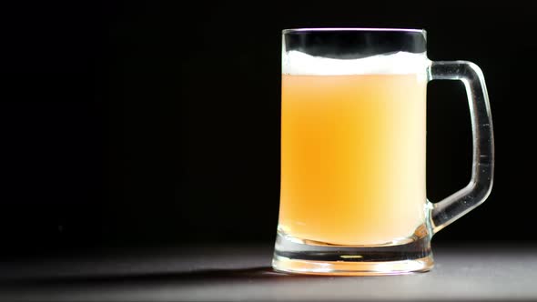 Big Glass Mug Full of Beer with Foam Slowly Rotating Isolated at Black Studio Background alt