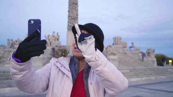 Asian woman standing and taking video call in public Frogner park, Norway alt