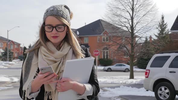 A Young Female Walking Outside In Winter Wearing A Scarf And Hat Looking At Smart Phone 2