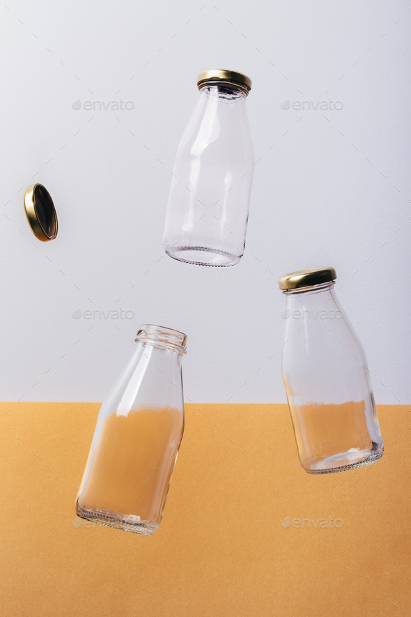 Glass bottles milk packaging falling down on white and orange background.