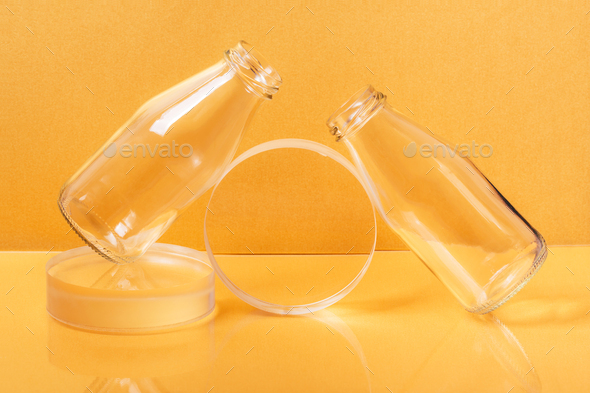 Glass bottles milk packaging on clear sphere shape stands on orange background. Creative minimalist still life