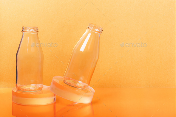 Glass bottles milk packaging on clear sphere shape stands on orange background.