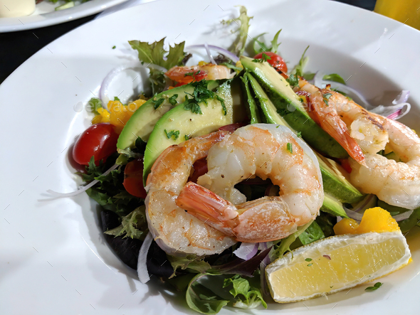 Prawns or shrimps and avocado served with a fresh garden salad and lemon on white plate
