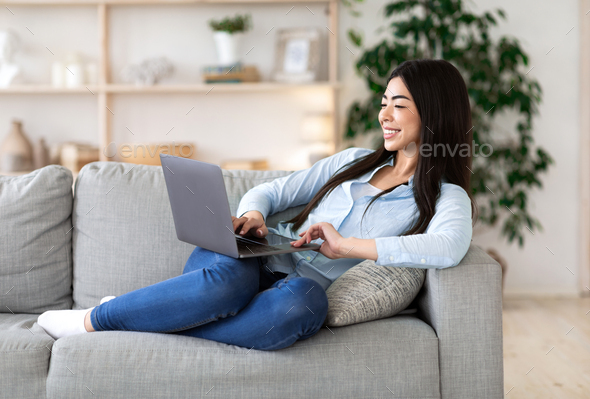 Favorite Pastime. Cheerful Asian Woman Relaxing With Laptop On Couch, Browsing Internet
