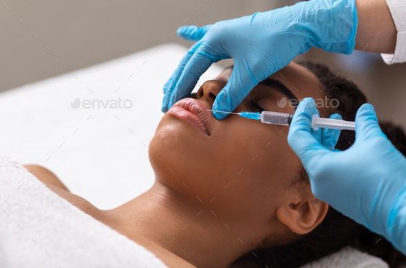 Black lady getting lip filling injection at beauty salon