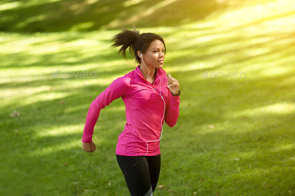 Athletic black girl jogging by public park