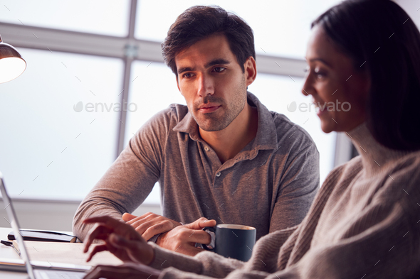Businesswoman Working On Laptop At Desk Collaborating With Male Colleague Drinking Coffee