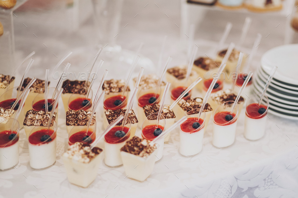 Delicious creamy panna cotta desserts with fruits, cakes and cookies on table at wedding reception