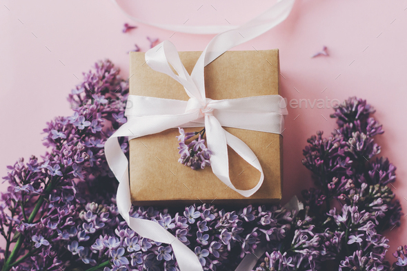 Lilac flowers and gift box on pink background