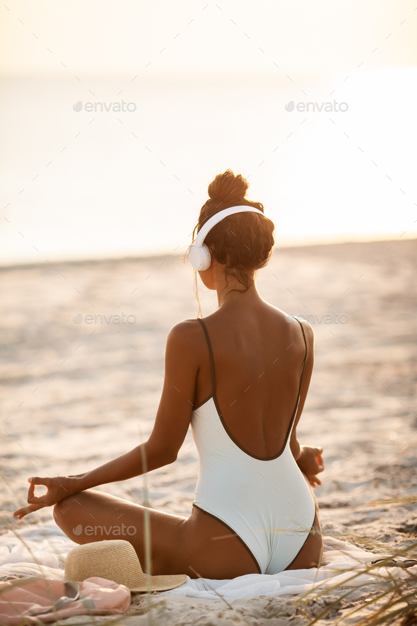 Woman in Yoga Meditation Pose with Headphones on the Beach
