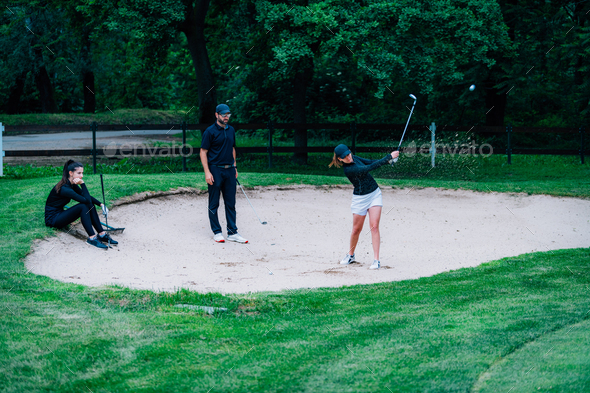 Golf lessons – Young woman having a golf lesson, playing from sand bunker