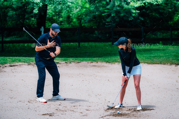 Golf lessons – Young woman having a golf lesson, playing from sand bunker