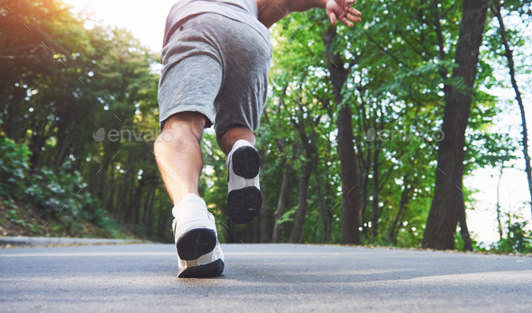 Close up of feet of young runner man running along road in the park