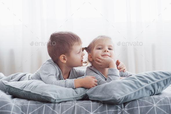Children wake up in sunny white bedroom. Boy and girl play in matching pajamas