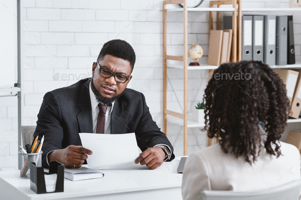 Job search. Serious HR manager looking through applicant's resume during employment interview at