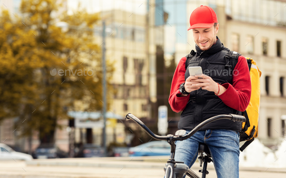 Courier Using Application On Smartphone Sitting On Bicycle In City