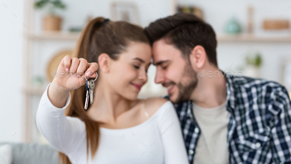 First home for young family. Happy husband and wife in living room, woman shows keys