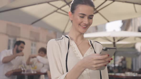 Happy Woman Using Mobile Phone At Street Bar