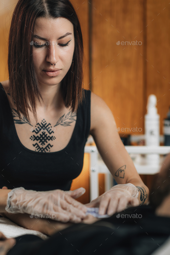 Tattooing. Female Tattoo Artist Applying Tattoo Stencil onto Male Arm before Tattooing