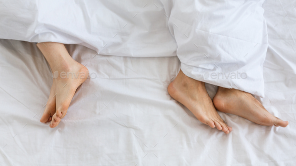 Problems in family relationship. Feet of man and woman in white bed at distance