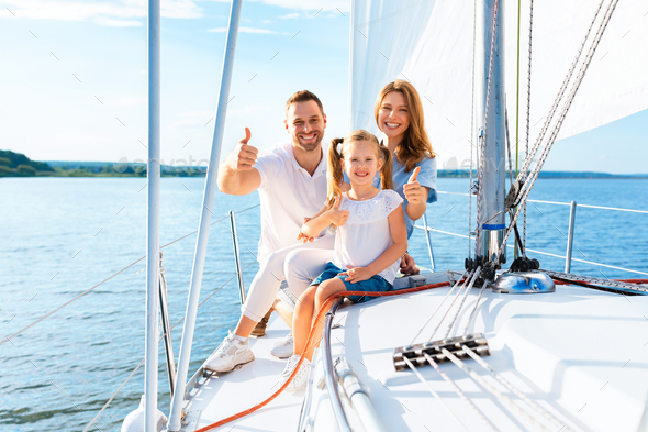 Family Gesturing Thumbs-Up Sitting On Deck Sailing Across Sea Outside