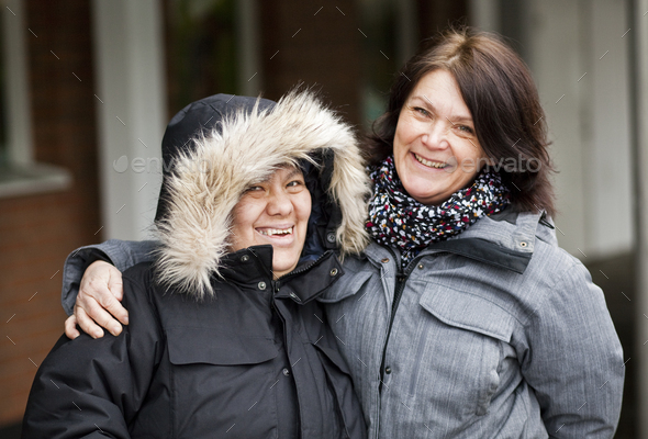 Portrait of happy caregiver with mentally disabled woman in warm clothing outdoors