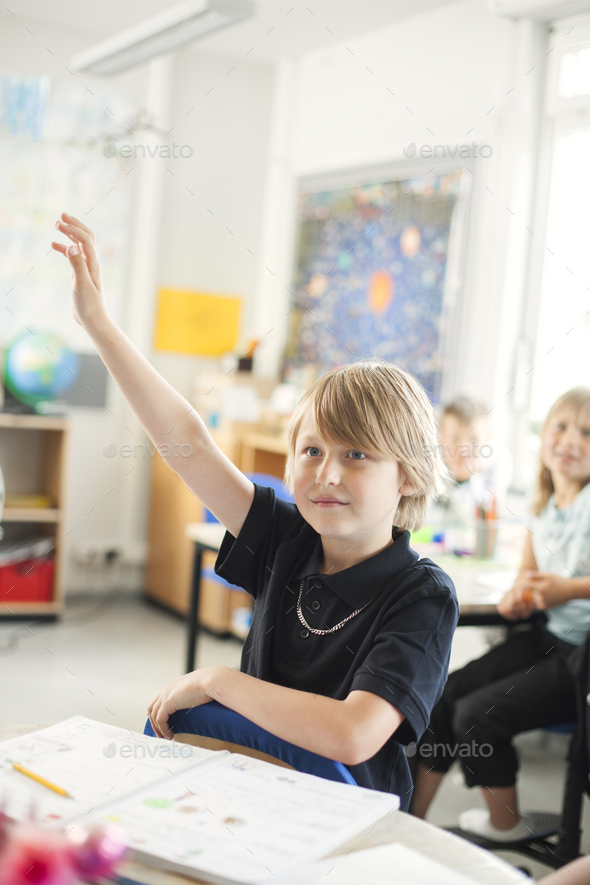 Schoolboy Raising Hand In Classroom Stock Photo By Astrakanimages 