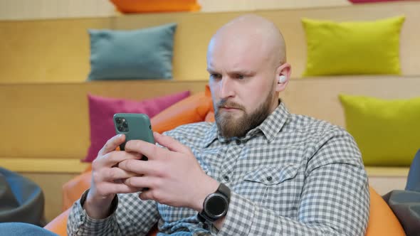 Close Up of an Young Man Sits on a Bean Bag While Playing Online Using His Phone alt