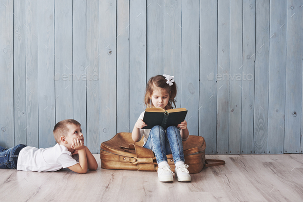 Happy little girl and boy reading interesting book carrying a big briefcase and smiling