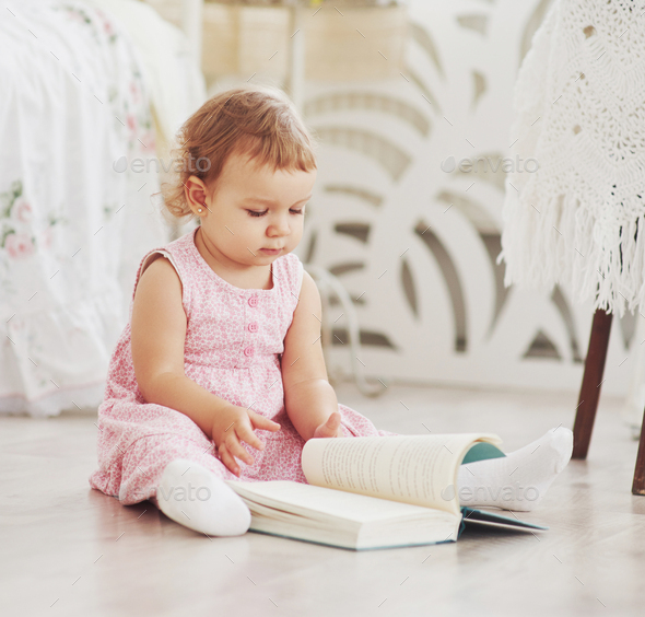Beautiful little girl read book with her favorite bear on a soft plush blanket